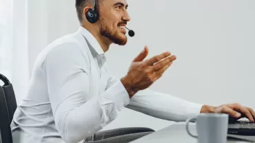 Person in white shirt smiling, using a laptop with headphones.