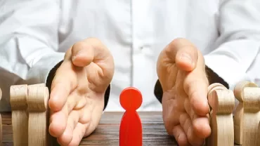 Hands separating a red figure from wooden figures on a table.