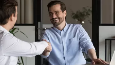 Two people smiling and shaking hands in an office setting.