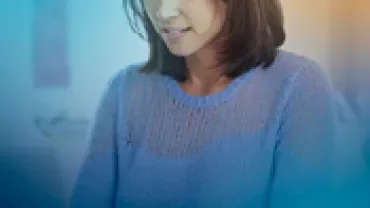 Person in a blue sweater working at a desk with a bright and blurred background.