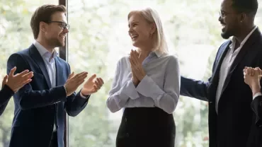 Colleagues cheerfully applauding a smiling person in an office.