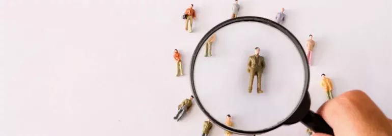Magnifying glass focusing on a small figurine among several others on a white background.