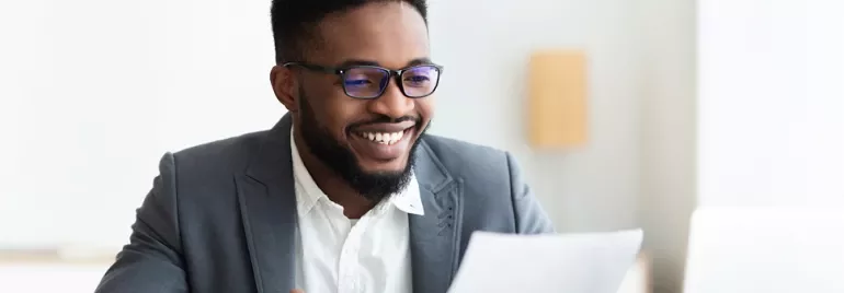 Person in a suit smiling while reading a document.