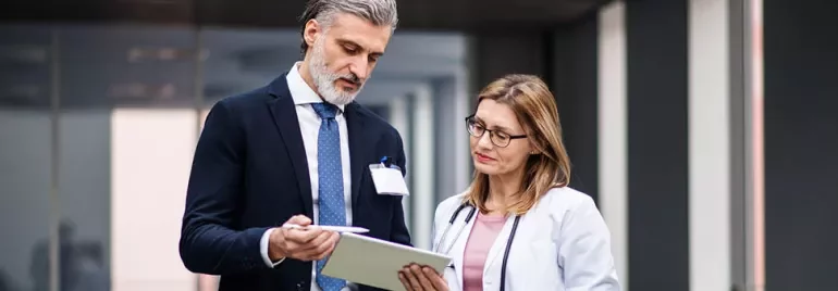 Two professionals discussing information on a clipboard in an office setting.